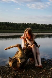 A thoughtful woman in a peaceful riverside setting during golden hour, embracing nature's tranquility.