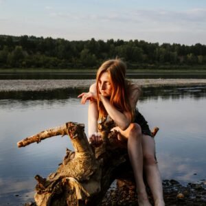 A thoughtful woman in a peaceful riverside setting during golden hour, embracing nature's tranquility.