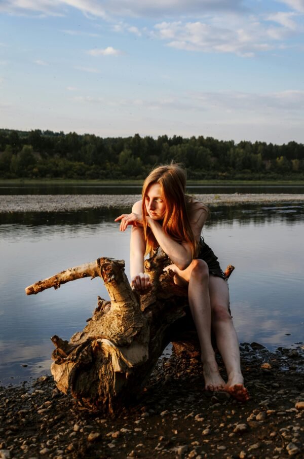 A thoughtful woman in a peaceful riverside setting during golden hour, embracing nature's tranquility.