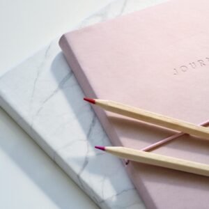 Close-up of a pink journal with pencils on a marble top. Perfect for note-taking or planning.